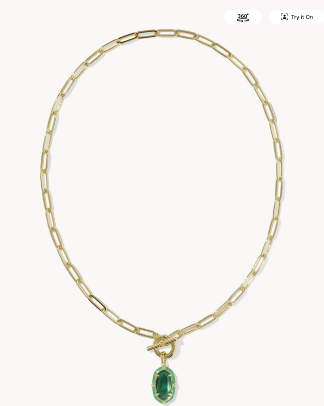 A gold paperclip chain necklace with a toggle clasp and a small oval green gemstone pendant, shown on a light gray background.
